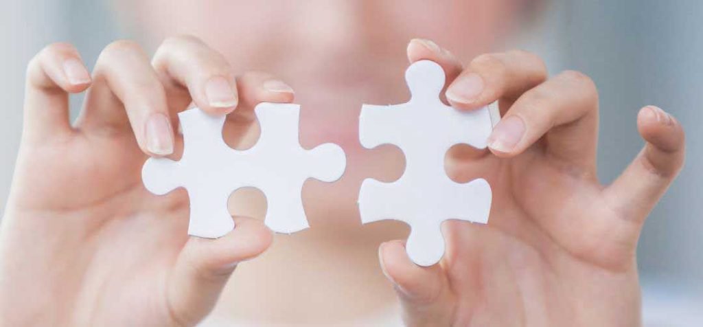 Hands holding two white puzzle pieces, almost connecting