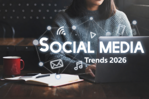 Woman using laptop at desk with notebook and coffee, overlaid with social media icons and “Social Media Trends 2026” text